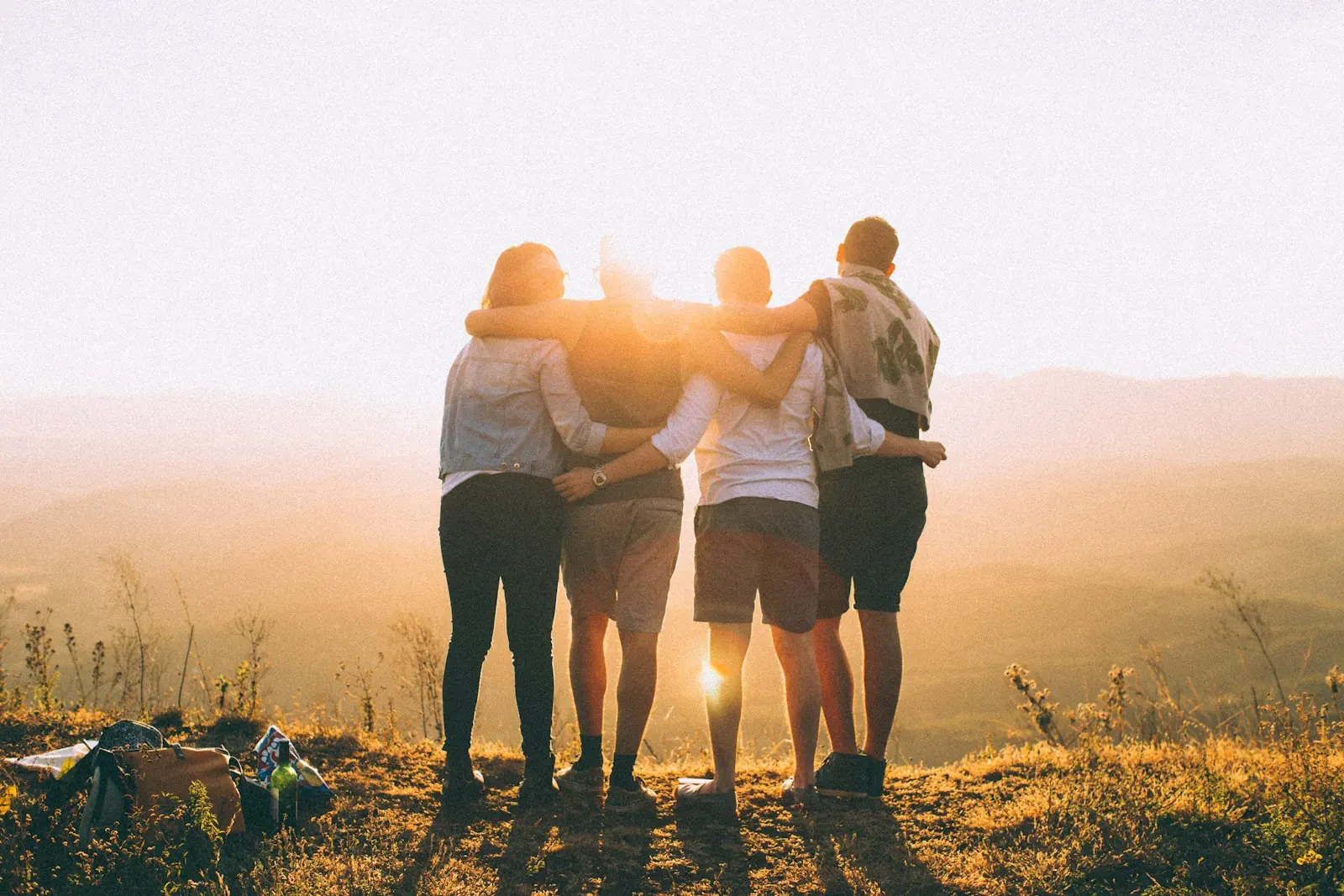 Four friends standing together outdoors at sunset (illustrative stock photo)